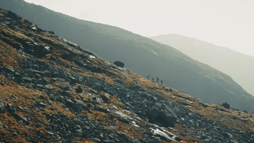 Group of people hiking and climbing a rocky mountain with the sun shining brightly on the horizon