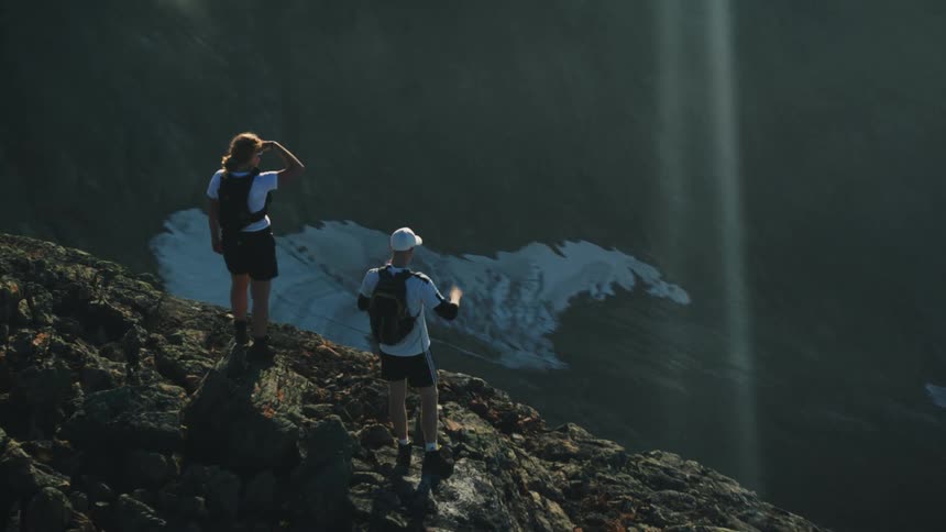 Two hikers stand on the top of a mountain and look down into an enormous valley