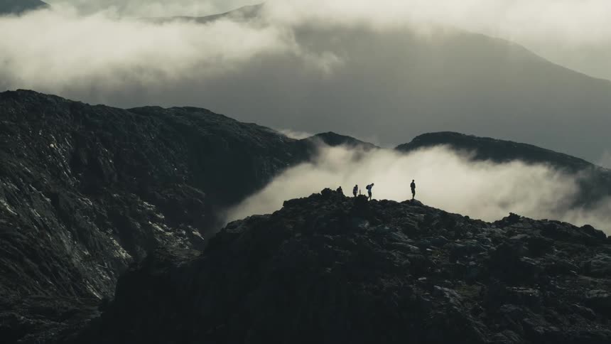 Individuals standing on a mountainous rock formation with low clouds