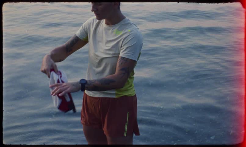 A woman in a white tshirt and red shorts stands on a lake wringing a hat