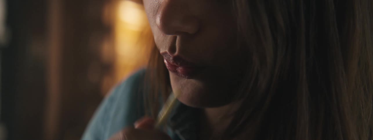 The mouth of a woman with long hair who is blowing a thin object and shaking it