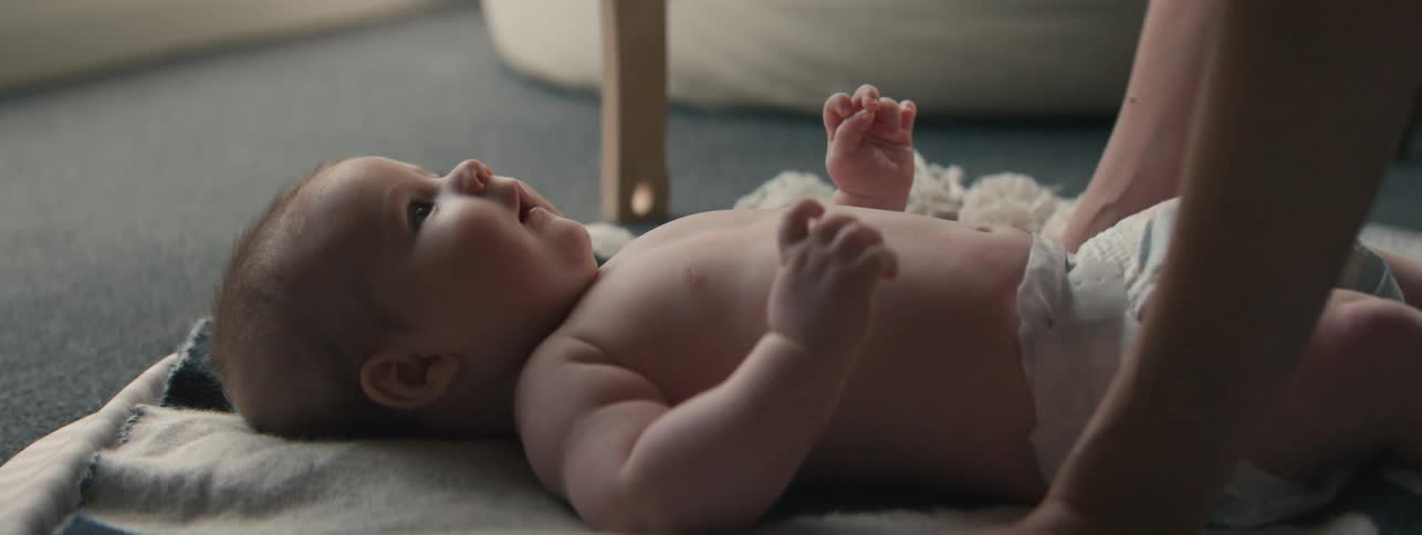 A mother leans towards her baby on the floor