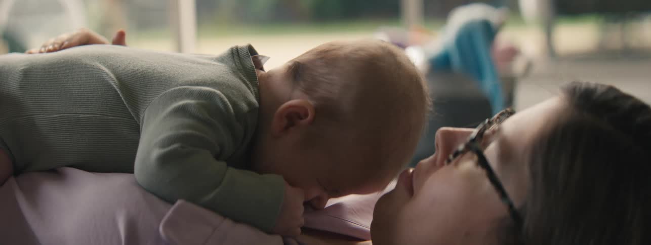 Mother lies on her back with a laughing baby on her chest