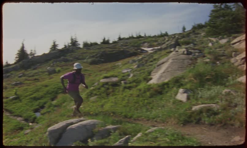A person in a white hat runs up a rocky hill