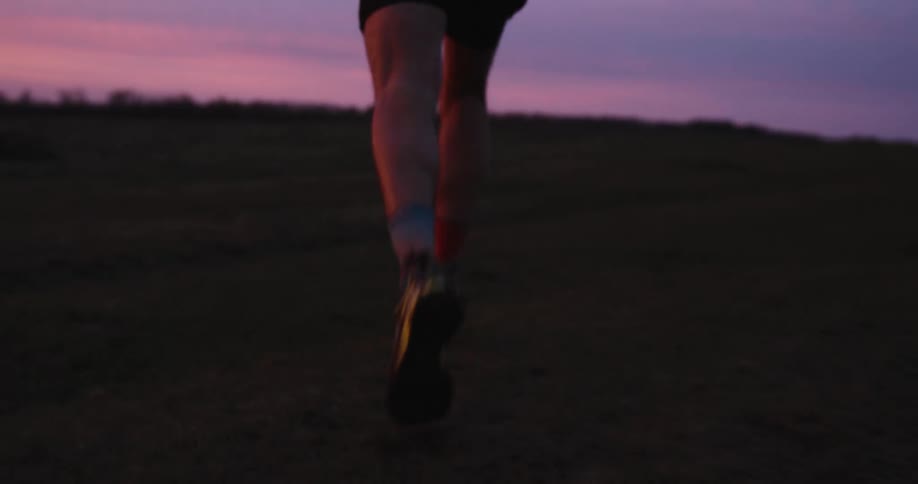 Legs of a person running in a field on a cloudy purplehued day