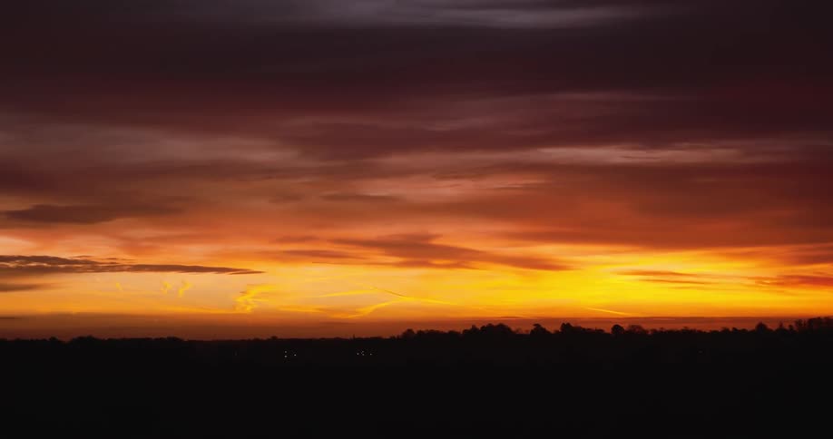 A fiery sunset paints the sky with shades of orange and red while a dark silhouette of trees lines the horizon