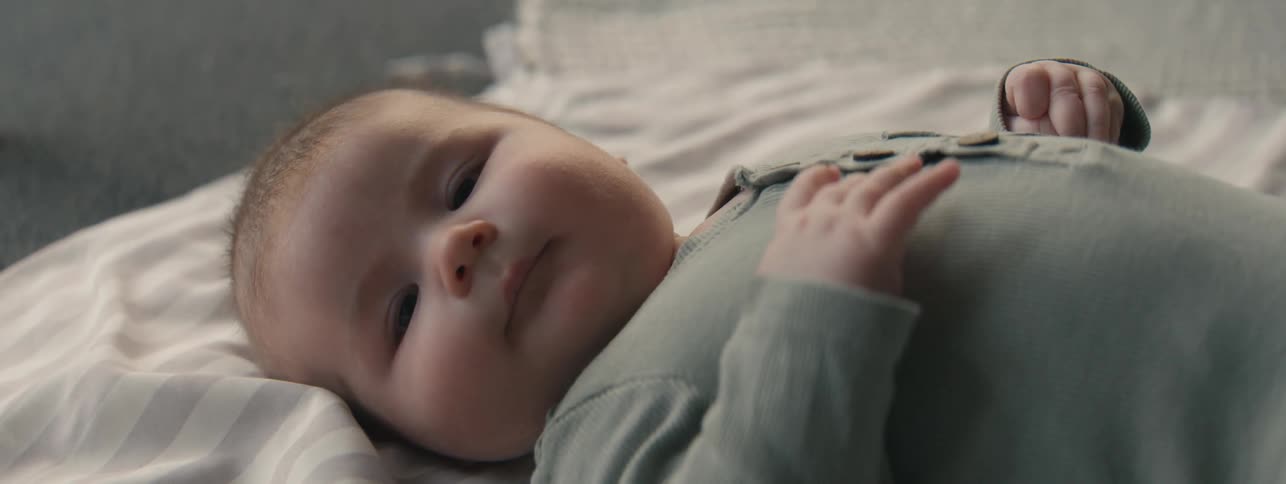 A baby lies on a white and grey striped blanket looking up with curiosity