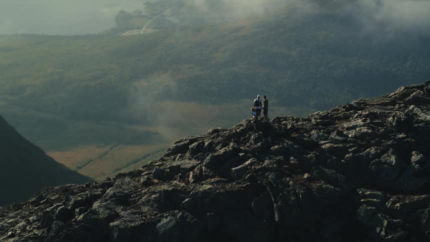 Individuals are standing on top of a rocky mountain with a vast landscape
