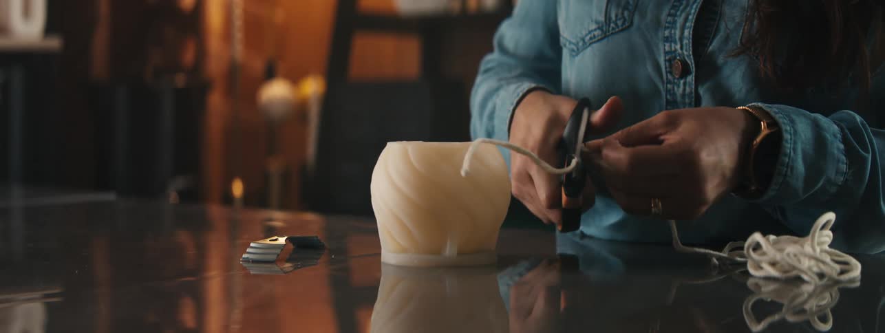 Female candle maker cuts the wick for a candle in her workshop