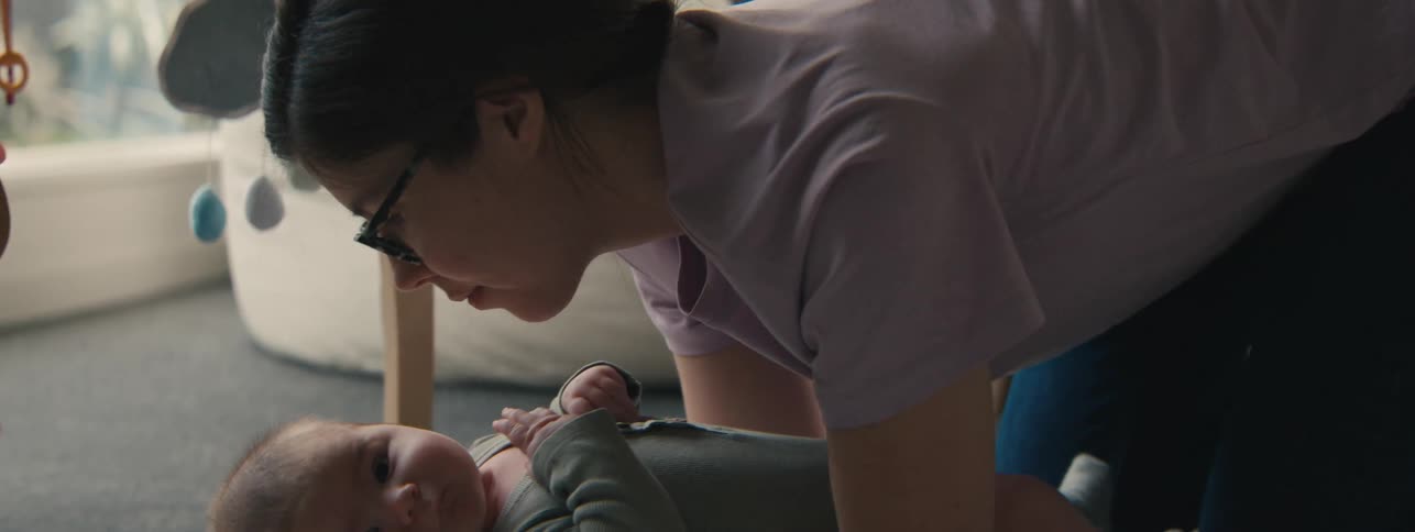 A woman with glasses holds a baby close to their face while lying on a lightcolored mat
