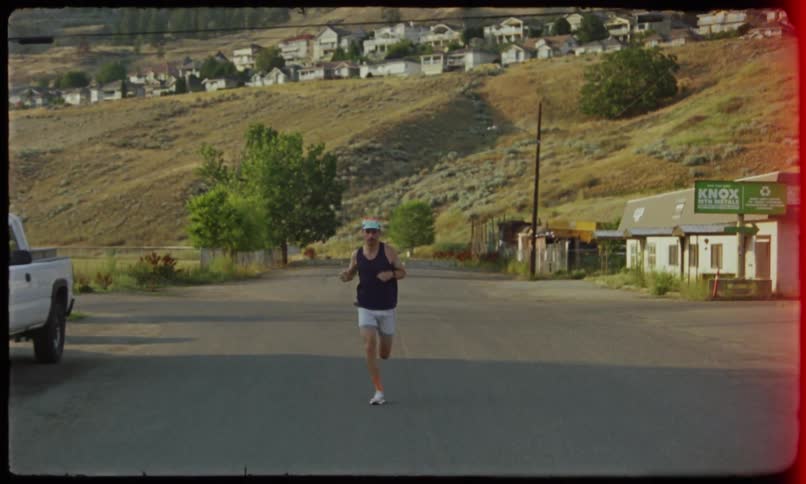 Man running on a paved street with a residential neighborhood in the background on hills