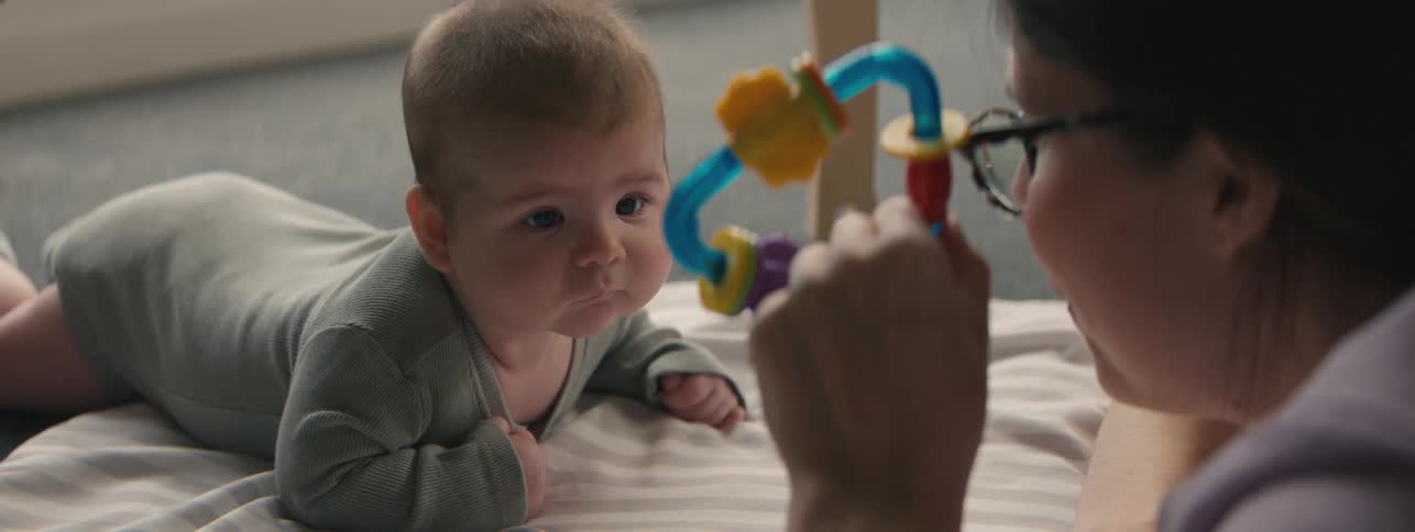 Mother holding a toy and playing with her newborn baby lying down
