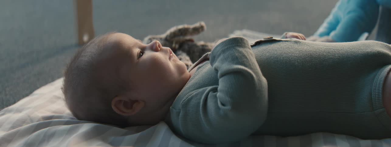 Baby lying on a blanket on the floor and interacting with toys by another person