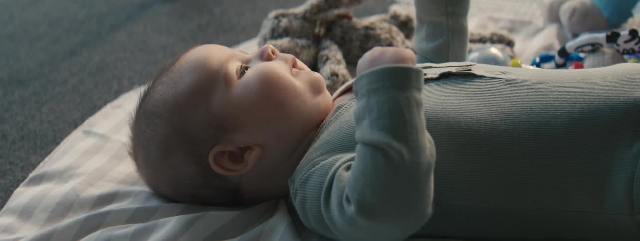 Newborn baby lying on a blanket on the floor and a hand with a toy interacting with him