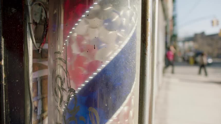 A faded barber pole sign hangs in the window of a shop on a city street