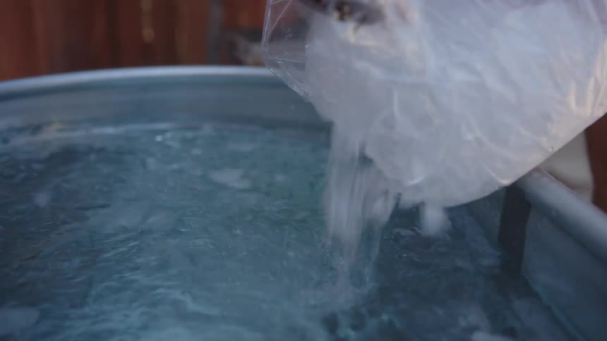 Person pouring a bag of ice into a bathtub