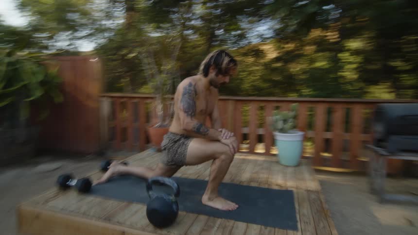 A man in a backyard porch doing leg stretches on a yoga mat
