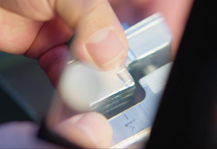 A close up of a hand holding a metallic machined object under a lens