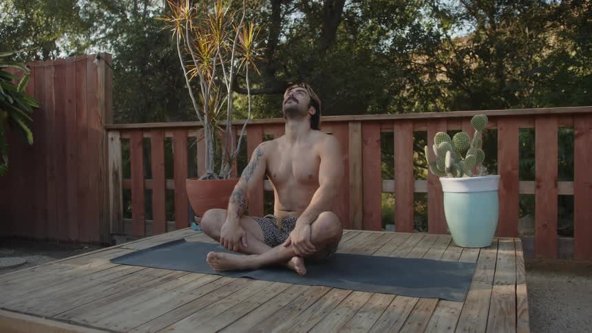 Man sitting on a wooden deck in yoga position relaxing