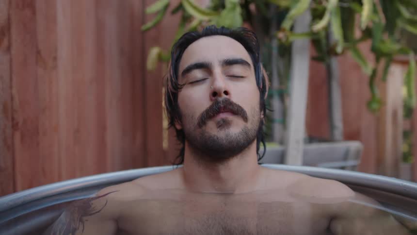 A man resting with his eyes closed in a tin bath tub