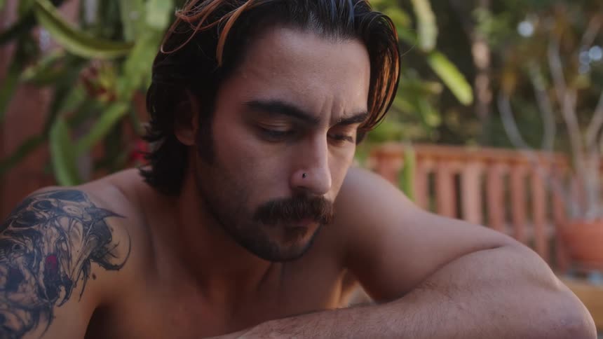 A man with a sleeve tattoo in a backyard rubs his hand over his hair
