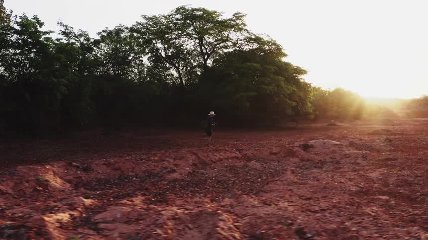 A man carrying a camera walking on a red soil clearing