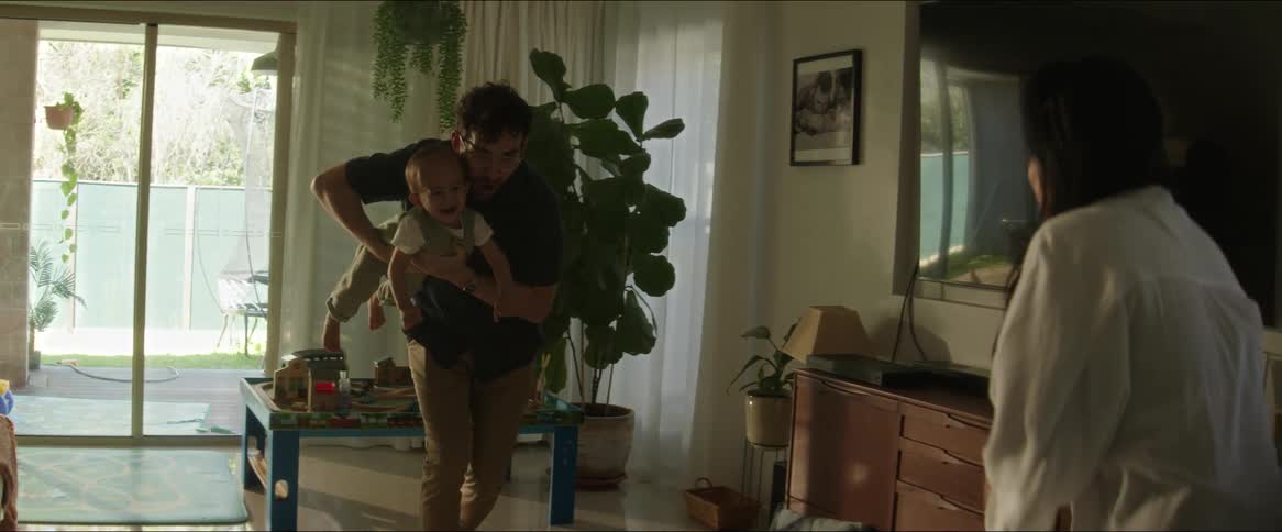 Father playing with a child on his lap and walking towards the mother