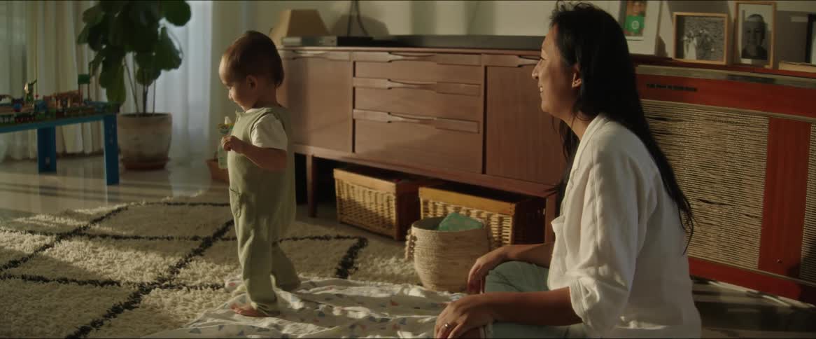 Mother sitting on the mat watching her little son learn to walk