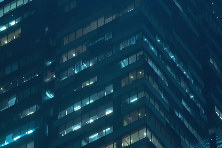 Looking up as window lights turn on all visible levels of a tall city building