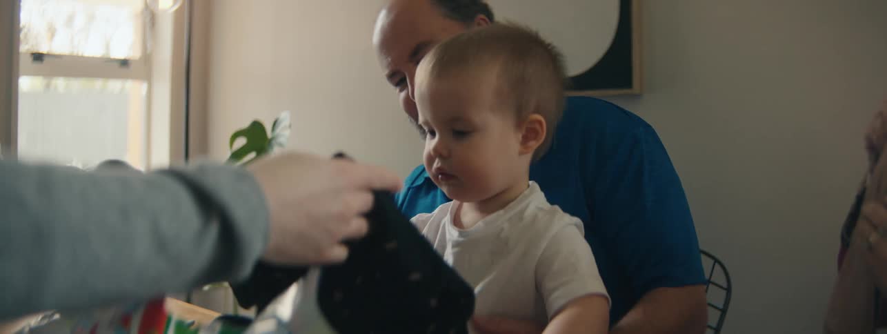 Small child sitting on fathers lap looking at clothes while sitting at table