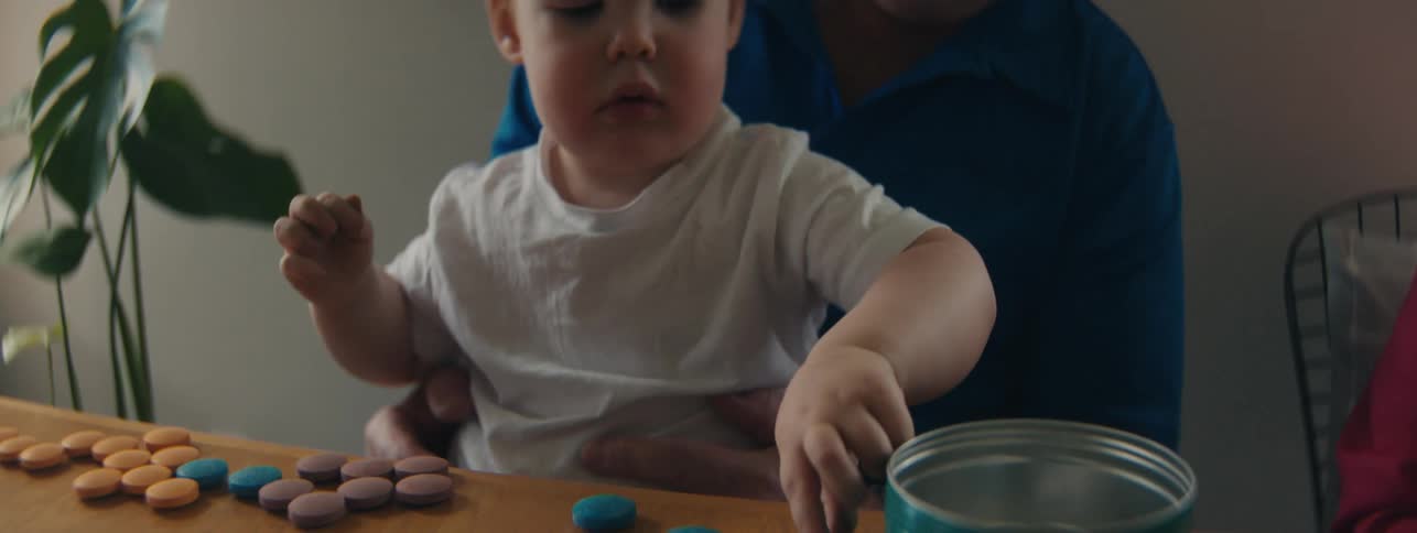 Grandfather holds child in his lap while the infant places objects into a metal container