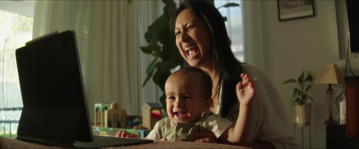 Mother sitting with her baby and both smiling in front of a laptop