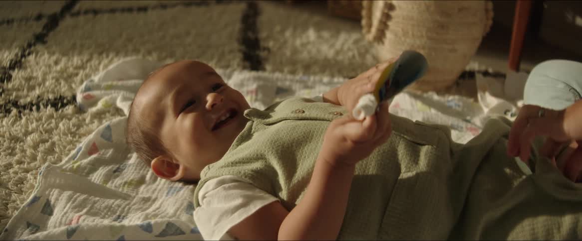 A mother touches her toddler son as he lies on a blanket on the floor