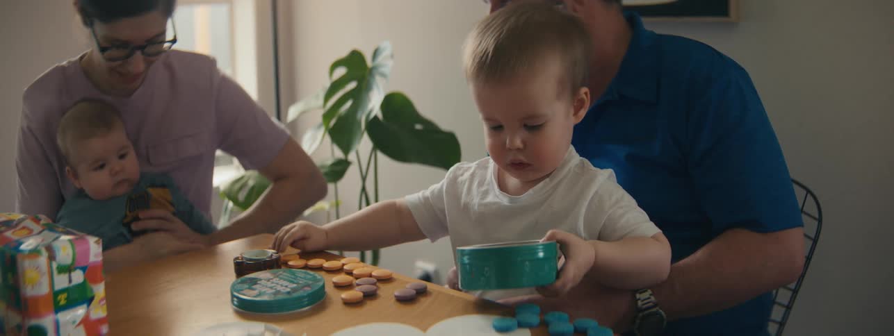A little child in a white shirt is on an adults lap and is playing with objects that are in a small green box