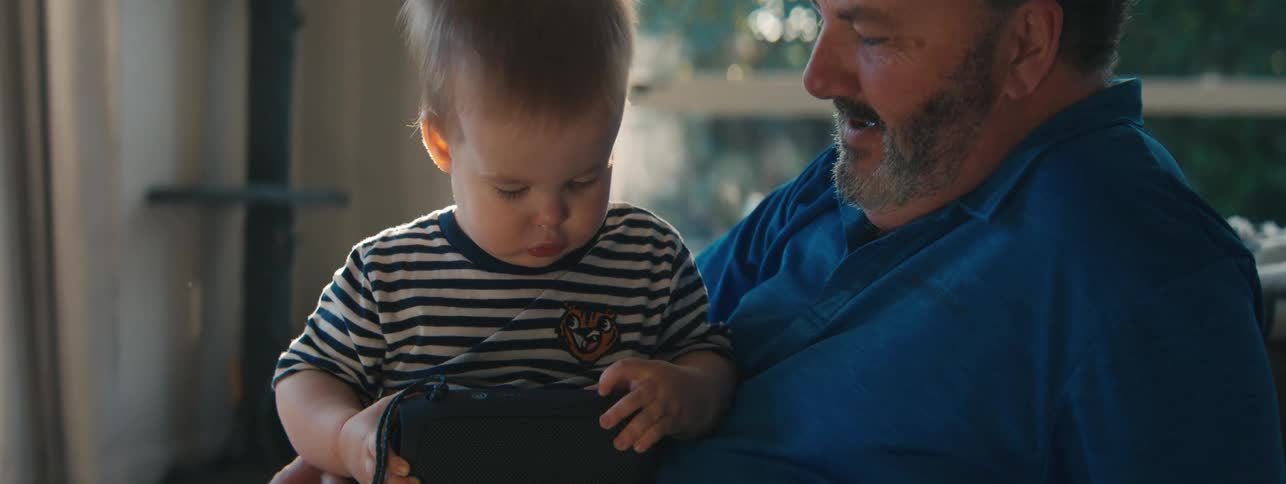 Man smiles while holding a boy focused on examining an object