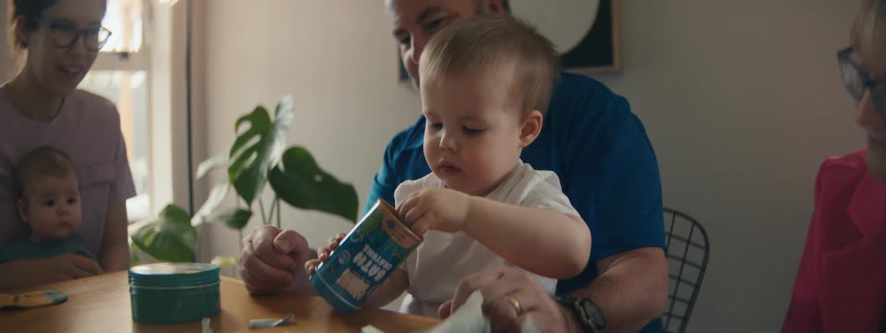 Family sitting together at a table with a child tearing open a gift wrapper