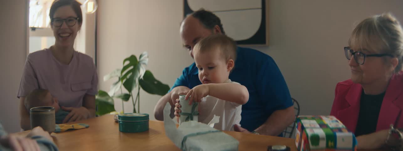 Family gathered at the table while a small child opens a box