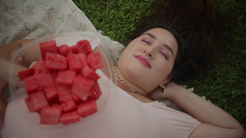 Woman lying on grass and refusing chopped watermelon