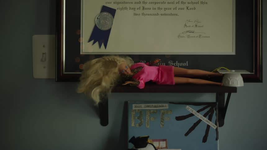 A doll lies on a small wooden shelf in front of a frame diploma hanging on a wall