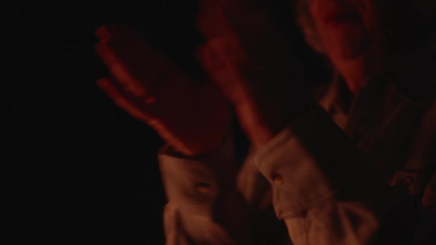 An elderly woman claps her hands while smiling in a dark area
