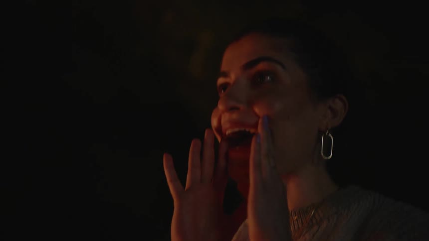 Smiling woman clapping her hands while standing outdoors at night