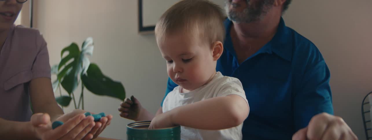 Small child playing at the table accompanied by his relatives