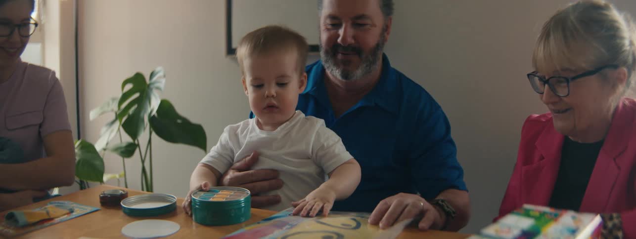 Child sitting on fathers lap at the table looking at the gift he received with his family around