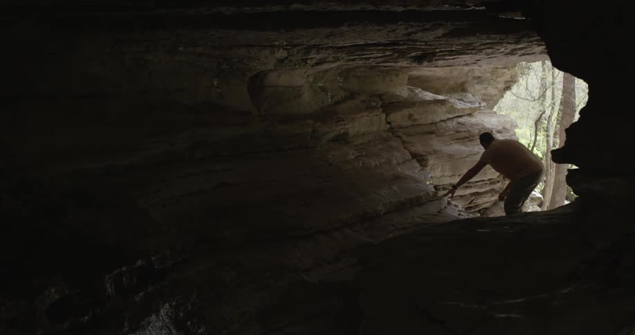 A man and woman climb into a cave