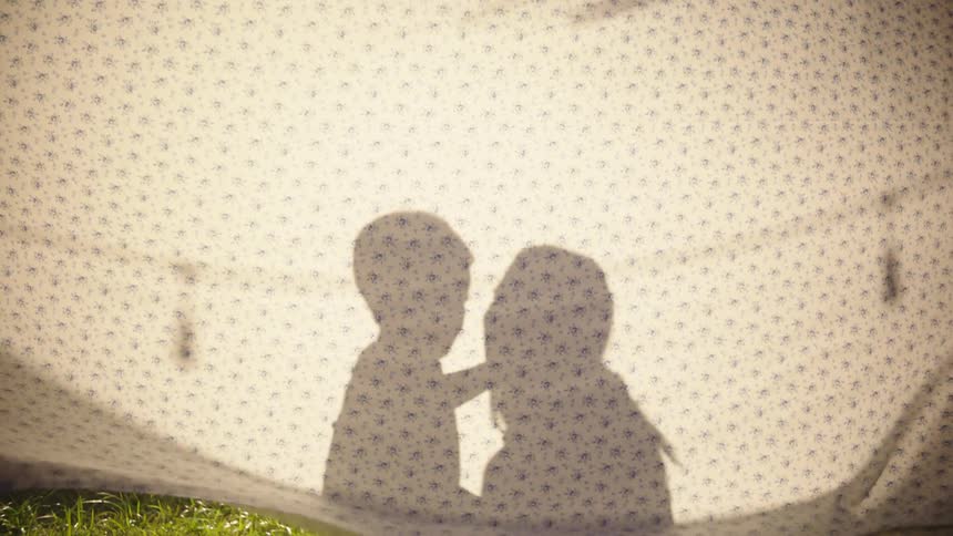 Behind a hanging sheet a woman gets down and embraces a baby that just walked to her