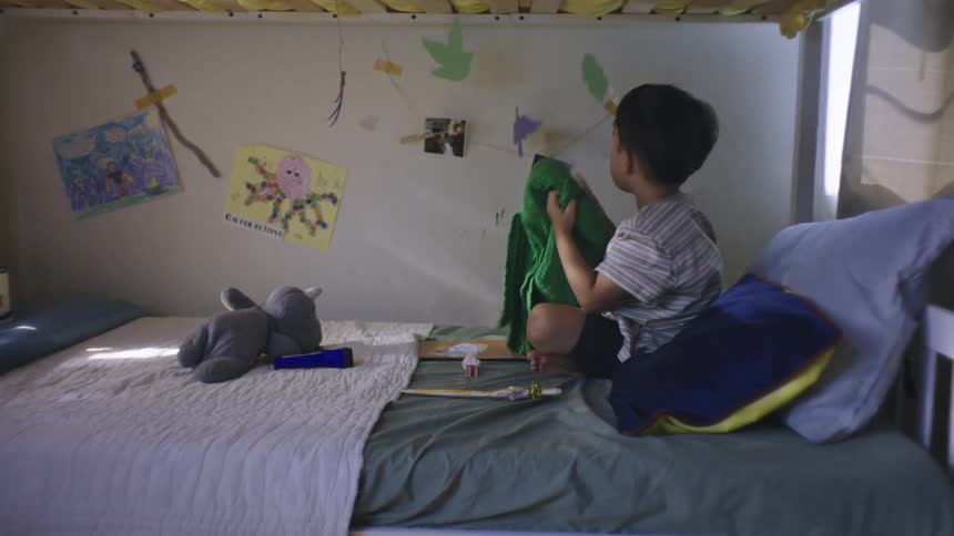 Boy sitting on bed grabbing blanket and looking at wall with decoration