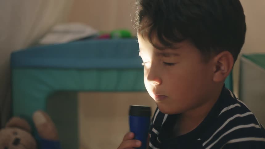 Boy sitting playing with a flashlight on his face