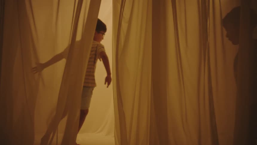 Two boys running and playing between curtains