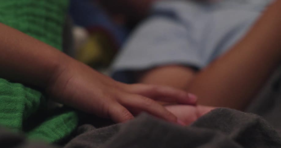 One boy touches his foot while another boy lies nearby in a bedroom