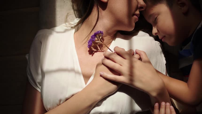 Mother lying down with her sleeping son holding a purple flower together